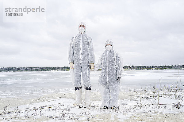 Vater und Sohn in Schutzanzügen am gefrorenen Fluss stehend