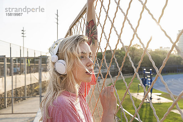 Junge Frau hört Musik an einem Maschendrahtzaun