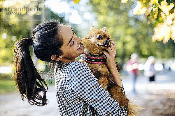 Glückliche junge Frau hält Hund in einem Park