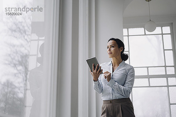Erfolgreiche Geschäftsfrau  am Fenster stehend  mit digitalem Tablet
