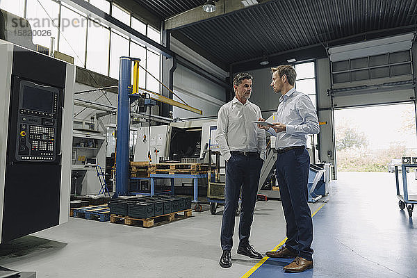 Zwei Männer mit Tablette im Gespräch in einer Fabrik