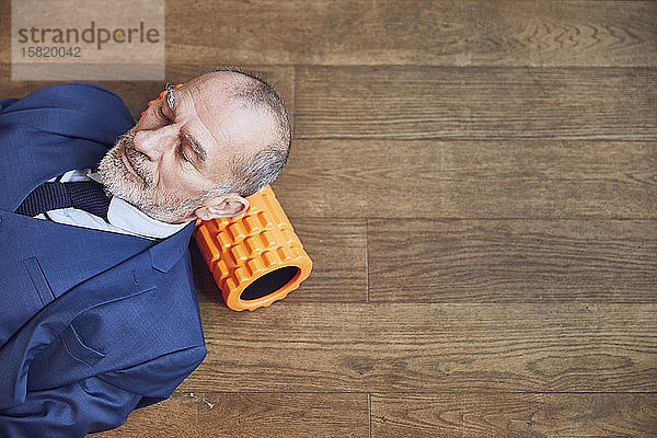 Älterer Geschäftsmann entspannt sich auf Holzboden  ruht auf Faszienrolle
