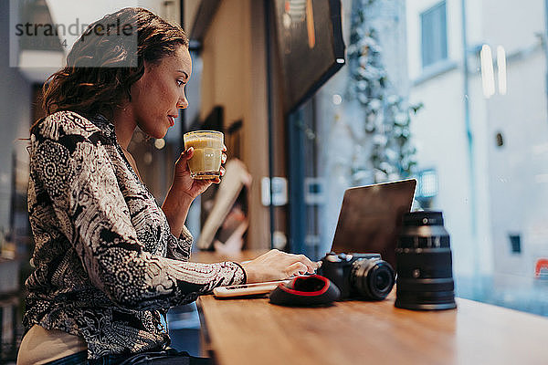 Junge Frau mit einer Kamera mit Laptop in einem Café hinter einer Fensterscheibe