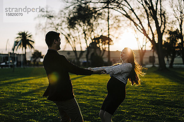 Glückliche werdende Eltern tanzen bei Sonnenuntergang in einem Park