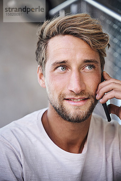 Porträt eines jungen Mannes mit T-Shirt beim Telefonieren
