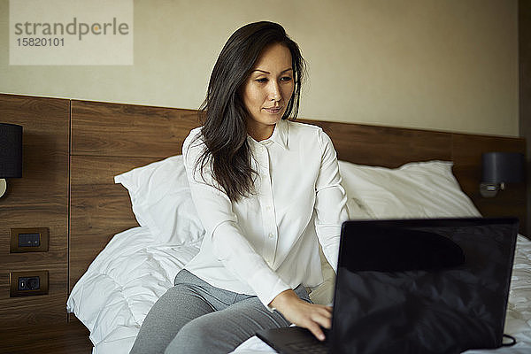 Geschäftsfrau sitzt mit Laptop im Hotelzimmer auf dem Bett