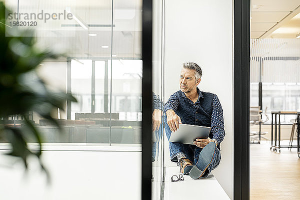 Gelegenheits-Geschäftsmann sitzt auf der Fensterbank eines Bürogebäudes und benutzt Laptp