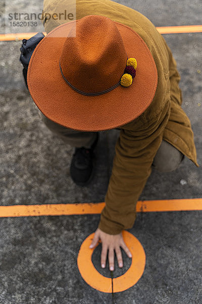 Draufsicht eines Mannes mit Hut  der seine Hand auf einen Kreis auf dem Boden legt