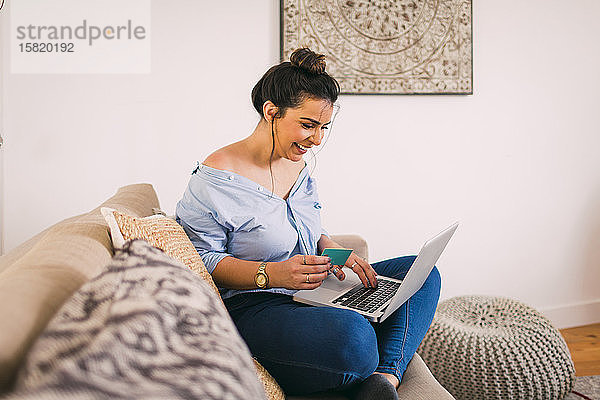 Lächelnde junge Frau beim Online-Shopping zu Hause