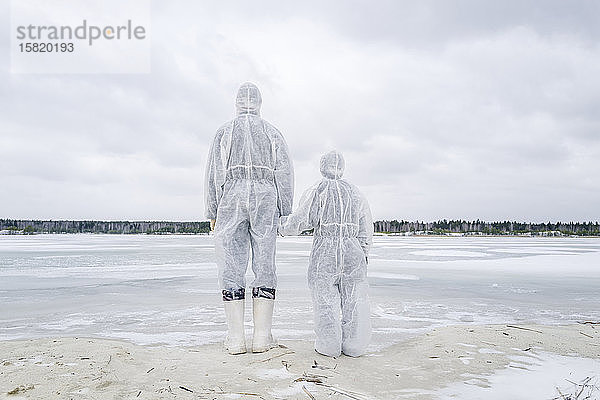 Rückansicht von Vater und Sohn in Schutzanzügen am gefrorenen Fluss stehend