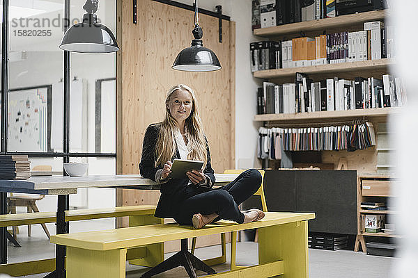 Junge Geschäftsfrau sitzt auf einer Bank in einem Loft-Büro und benutzt ein Tablett