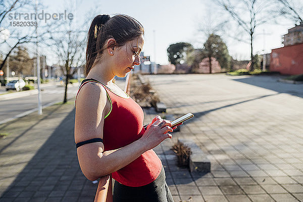 Sportliche junge Frau mit Smartphone in der Stadt