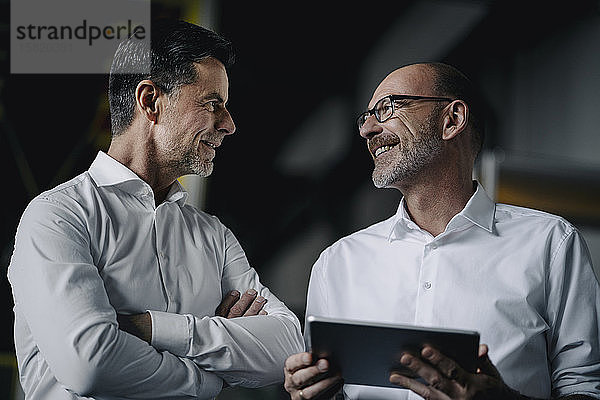 Zwei lächelnde Männer mit Tablette im Gespräch in einer Fabrik