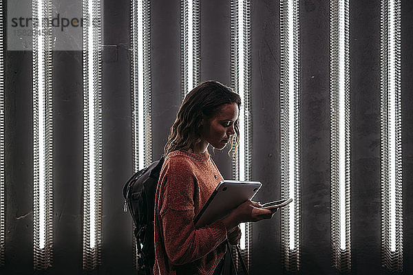 Junge Frau benutzt Smartphone an beleuchteter Wand