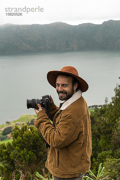 Porträt eines lächelnden Mannes mit Kamera an einem See stehend  Sao-Miguel-Insel  Azoren  Portugal