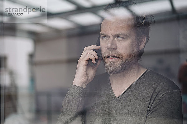Porträt eines Geschäftsmannes am Telefon hinter einer Fensterscheibe