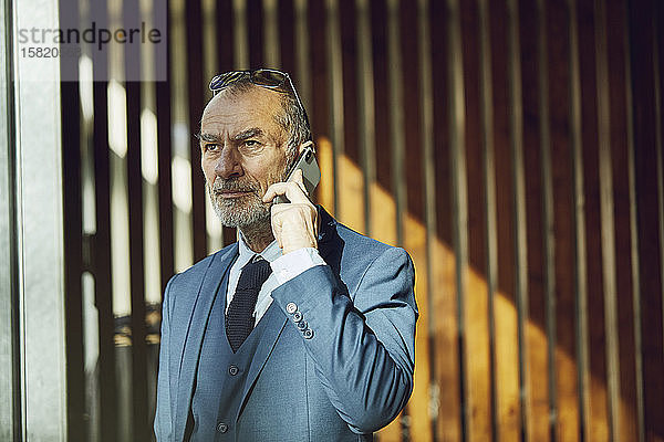 Leitender Geschäftsmann steht in seinem nachhaltigen Büro und spricht am Telefon