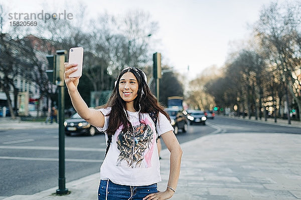 Junge Frau mit Kopfhörern  die einen Selfie mit ihrem Smartphone macht