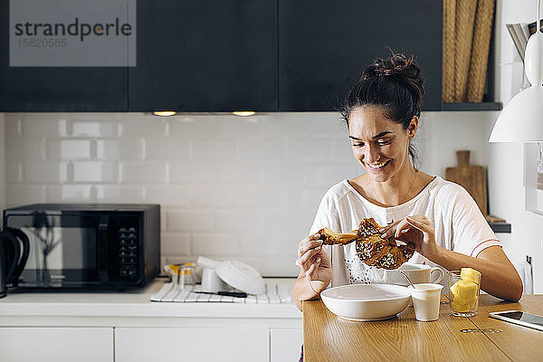 Glückliche junge Frau beim Frühstück in der Küche