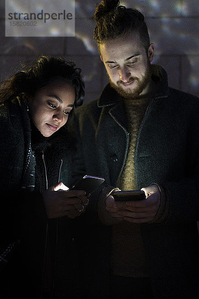 Ehepaar betrachtet beleuchtete Smartphones im Dunkeln