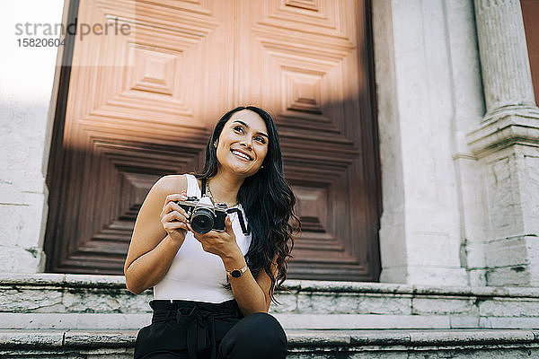 Porträt einer glücklichen jungen Frau  die auf einer Treppe sitzt und mit der Kamera fotografiert  Lissabon  Portugal