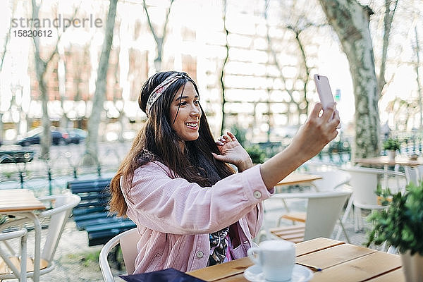 Junge Frau sitzt am Freilufttisch und macht ein Selfie