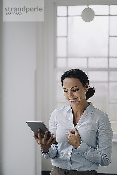 Erfolgreiche Geschäftsfrau  am Fenster stehend  mit digitalem Tablet  lächelnd
