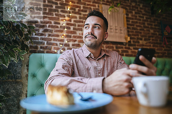 Porträt eines Mannes in einem Cafe mit einem Mobiltelefon