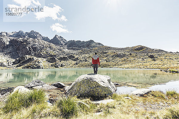 Rückansicht eines jungen Mannes auf einem Felsen mit Blick auf einen klaren Bergsee