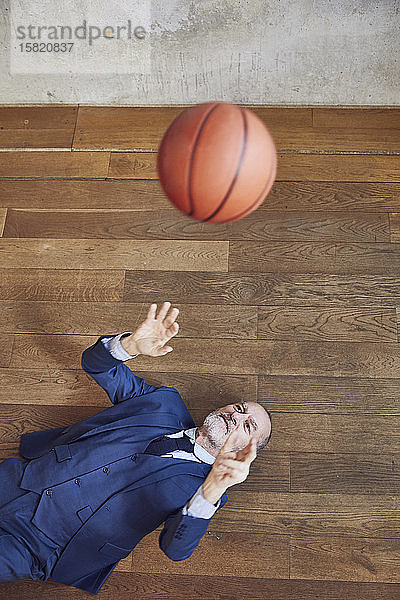 Leitender Geschäftsmann auf Holzboden liegend  mit Basketball spielend