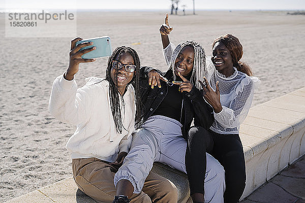 Porträt von glücklichen Teenager-Freundinnen  die am Strand ein Selfie machen