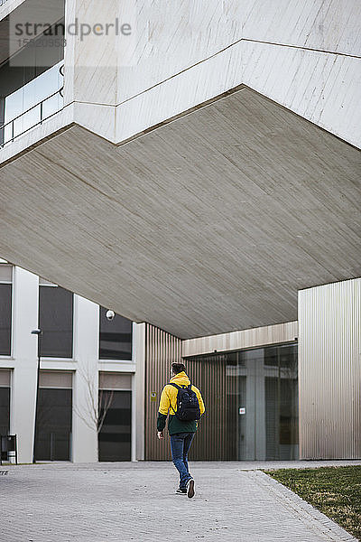 Rückansicht eines Mannes mit Rucksack beim Spaziergang entlang eines Gebäudes in der Stadt