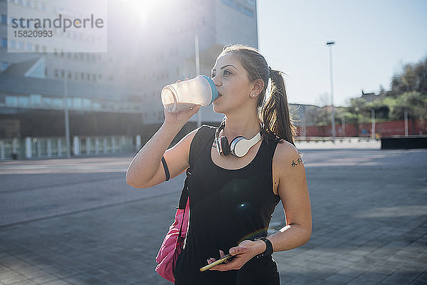 Sportliche junge Frau trinkt in der Stadt aus der Tasse