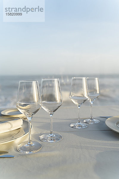 Spanien  Leere Weingläser auf gedecktem Restauranttisch mit Meer im Hintergrund