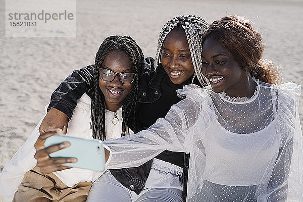 Porträt von glücklichen Teenager-Freundinnen  die am Strand ein Selfie machen