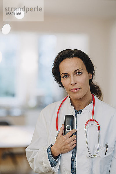 Weibliche Doktoe  die im Hosptal steht und Telefon und Stethoskop hält