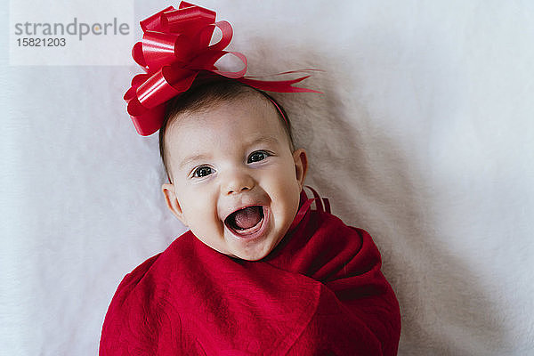 Porträt eines glücklichen Mädchens mit roter Schleife auf dem Kopf  eingehüllt in eine rote Decke