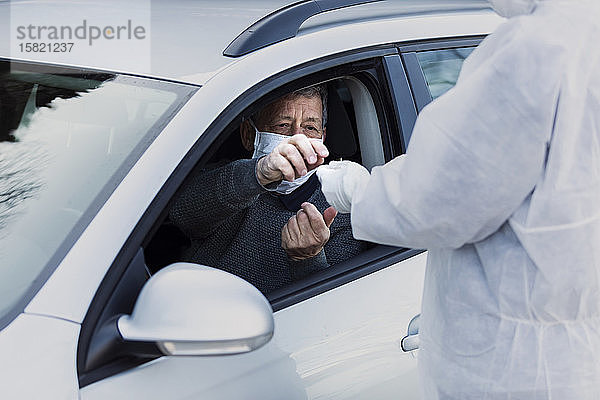 Mann in Schutzkleidung kontrolliert älteren Mann im Auto