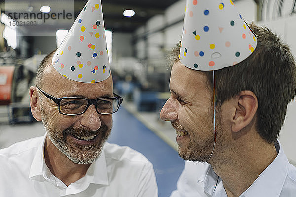 Porträt von zwei glücklichen Geschäftsleuten mit Partyhüten in einer Fabrik