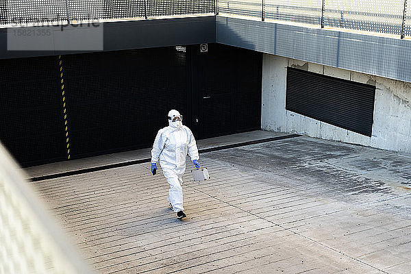 Wissenschaftlerin  die Schutzanzug und Maske trägt und in eine Garage geht