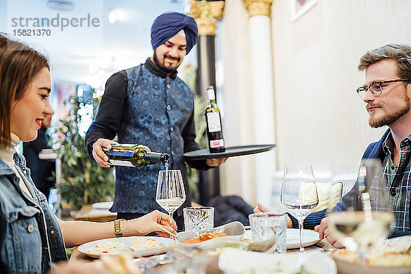 Freunde essen in einem indischen Restaurant  Kellner gießt Wein in Gläser