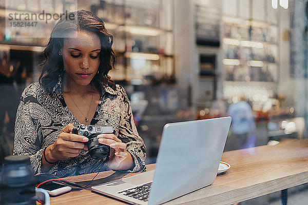 Junge Frau mit Kamera und Laptop in einem Café hinter einer Fensterscheibe