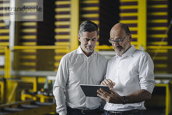 Zwei Geschäftsleute verwenden Tabletten in einer Fabrik