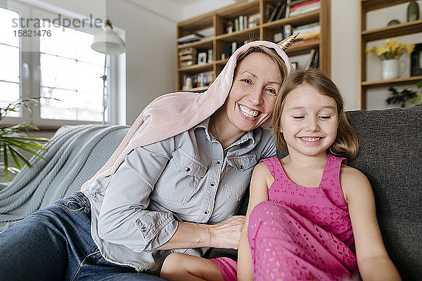 Porträt einer glücklichen Mutter und ihrer kleinen Tochter  die zusammen auf der Couch sitzen und Spaß haben