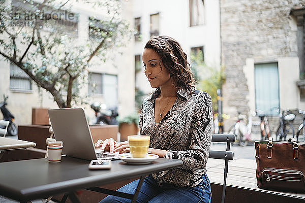 Junge Frau mit Laptop in einem Straßencafé