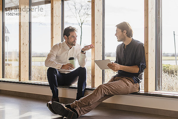 Zwei Geschäftsleute mit Tablett am Fenster im Großraumbüro im Gespräch