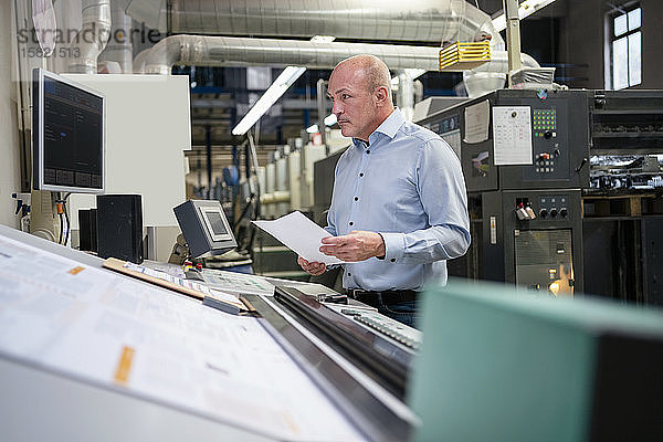 Geschäftsmann hält Papier an einer Maschine in einer Fabrik