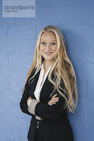 Porträt einer lächelnden jungen Geschäftsfrau an einer blauen Wand