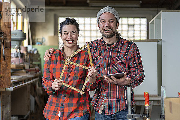 Porträt einer glücklichen Handwerkerin und eines Handwerkers  die in ihrer Werkstatt Tafel und Messlatte halten