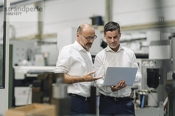 Zwei Geschäftsleute mit Laptop in einer Fabrik